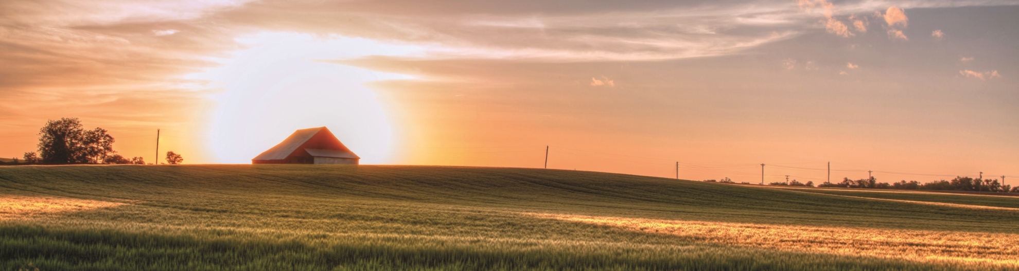 Descending sun illuminates a barn on top of a hill